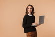 © Drobot Dean - Photo of cute woman 20s standing and holding laptop, isolated over beige background