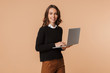 © Drobot Dean - Photo of european woman 20s standing and holding laptop, isolated over beige background