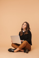 Sticker - Image of charming woman 20s using laptop, while sitting on floor isolated over beige background