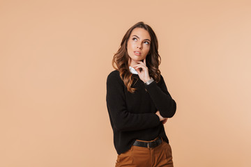 Wall Mural - Image of european woman 20s thinking and touching chin with brooding glance, isolated over beige background