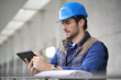 © goodluz - Handsome building expert in hardhat outdoors with tablet and blueprint