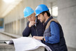 © goodluz - Workmen in hard hats consulting over blueprint on modern building sight
