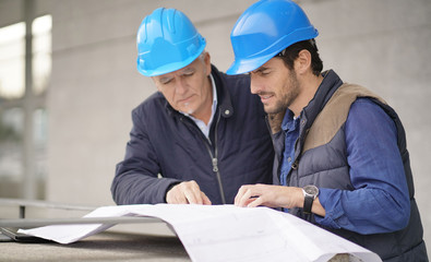 Workmen in hard hats consulting over blueprint on modern building sight