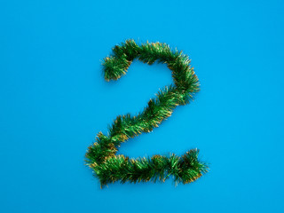 number two 2 made of green Christmas tree tinsel on blue background