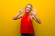 © luismolinero - Young girl with red dress over yellow wall counting eight with fingers