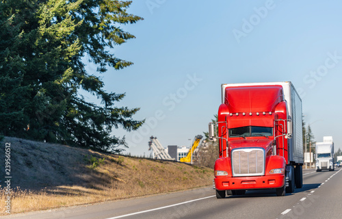 Obraz Dibond Big rig, jasnoczerwona, klasyczna amerykańska idolowa ciężarówka z naczepą chłodniczą jadącą prostą autostradą w słoneczny dzień