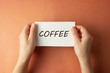 © Inga - Coffee inscription. Woman holding paper with Coffee lettering in hands isolated brown background. Top view. Minimalist style.
