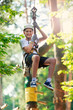 © Natali - Child in forest adventure park. Kid in white helmet  and white t shirt climbs on high rope trail. Agility skills and climbing outdoor amusement center for children. young boy plays outdoors