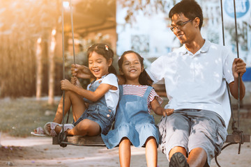 Wall Mural - Asian father and daughter having fun to ride on swings together in playground at the park