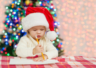 Baby girl in red christmas hat writes letter to Santa Claus. Empty space for text