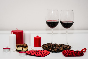 A romantic dinner with candles for Valentine's Day. Cake, glasses of wine. The heart of coffee beans. Decorated red hearts on background. Card, romantic composition love. space for text. side view.