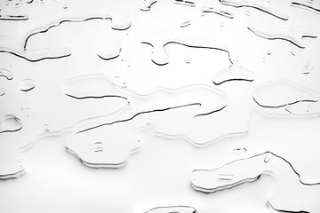 Drops of spilled water on white glass surface, silhouettes of water blots, abstract design element, textured background, black and white monochrome color, close up, top view