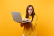 Portrait of bewildered young woman in fur sweater and heart eyeglasses working on laptop pc computer isolated on bright yellow background. People sincere emotions, lifestyle concept. Advertising area.
