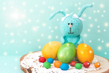 Easter celebration. Cute handmade knitted hare - a symbol of the holiday. Near her are colored eggs and Easter cake. Free space for text. Greeting card.