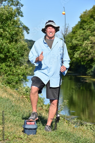 Fotografie, Obraz Older Retiree Adult Male Fisherman With Thumbs Up With Rod And Reel Outdoors