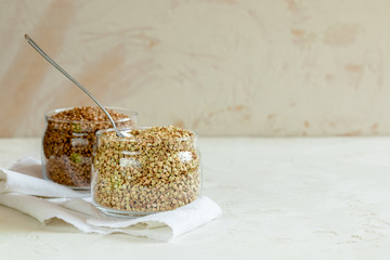 Two cans of buckwheat and spoon on white table with copy space.