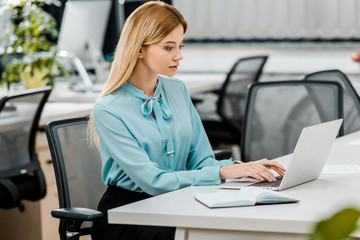 side view of young businesswoman working on laptop at workplace with notebook in office