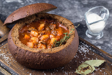 Goulash served in a bread bowl with cream on black background