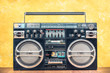 Retro outdated portable stereo boombox radio receiver with cassette recorder from circa 80s front concrete textured yellow wall background. Listening music concept. Vintage old style filtered photo