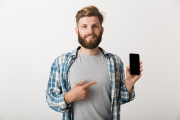Handsome young bearded man standing isolated over white wall background using mobile phone.