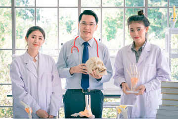 A handsome professor doctor teaching couple of beautiful young asian girl collage student in white laboratory gown learning anatomy class.  Anatomic bone of  hand in biology classroom in university.