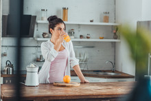 Young Woman Drinking Orange Juice In Kitchen During Morning Time At Home