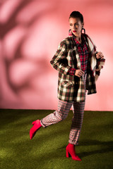 Wall Mural - attractive young woman posing in checkered suit on pink background