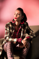 Wall Mural - beautiful stylish girl in checkered suit posing in armchair on pink background