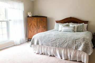 New bed comforter with headboard, decorative pillows, window, in bedroom in staging model home, house interior sunlight