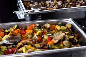 Fresh grilled vegetables in hot buffet tray with closeup of spoon to serve food to plate in banquet, wedding, or restaurant catering inside