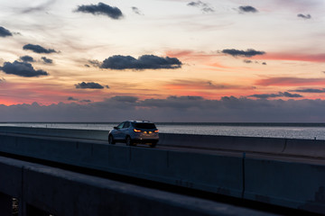 Wall Mural - Sunrise in Islamorada, Florida Keys, with red orange yellow sky, car on overseas highway road, in Atlantic Ocean, dark horizon
