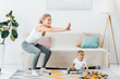 © LIGHTFIELD STUDIOS - attractive mother doing squats and cute toddler son sitting on carpet and playing with multicolored cubes at home