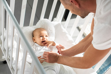 cropped view of father putting infant daughter into baby crib