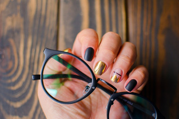 Luxury short manicure on a dark wooden background. Black matt nails design with golden color. 