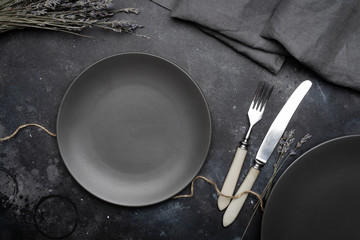 Empty gray plate (ceramic) on a dark gray background with a knife and fork, decorated with a bouquet of lavender and a napkin. Gray minimalistic concept. Copy space.