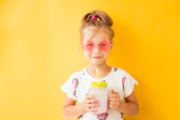 Little girl standing with milkshake in hand on yellow background