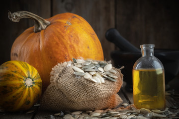 Wall Mural - pumpkin seeds oil bottle, two pumpkins, bag of seeds and mortar on background.