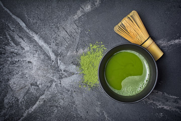 Top view on organic green matcha tea in black ceramic cup with bamboo whisk