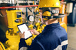 © dusanpetkovic1 - Young Caucasian worker in protective suit using tablet while checking machines in heating plant.