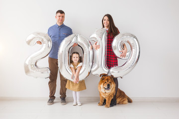 New year, celebration and holidays concept - family holding sign 2019 made of silver balloons for new year in white room background