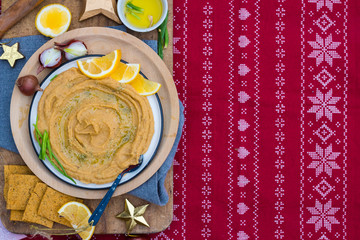 Chickpea hummus dip paste with corn crispy bread, olive oil. Space for text. Christmas food lunch or dinner on red background tablecloth with decoration on wooden board. Vegan vegetarian healthy food