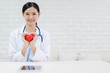 © anon - Young woman doctor holding a red heart, standing on brick wall background