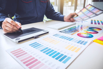 Poster - Male creative graphic designer working on color selection and color swatches, drawing on graphics tablet at workplace with work tools and accessories