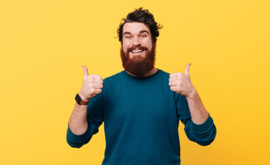 Wall Mural - Portrait of happy man showing thumbs up over yellow background