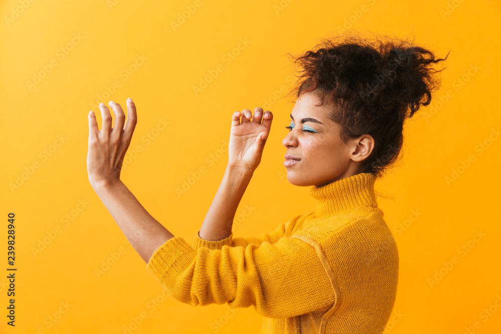 Portrait of beautiful african american woman with afro hairstyle looking through invisible spyglass, isolated over yellow background - obrazy, fototapety, plakaty 