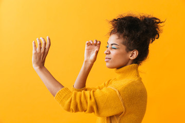 Poster - Portrait of beautiful african american woman with afro hairstyle looking through invisible spyglass, isolated over yellow background