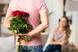 © Syda Productions - couple, relationships and people concept - happy woman looking at man hiding bunch of roses behind his back