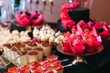 Wall Mural - Candy bar table set. Cookies, eclairs, macaroons, fruits, cream and layered cakes. Black, golden and red colours.