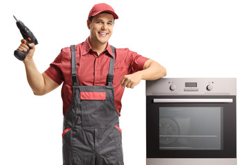 Wall Mural - Repairman with an electric drill standing next to an oven isolated on
