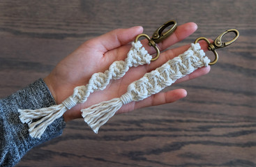 A hand holding up two hand-made macrame key chains that are made out of 100 percent cotton.